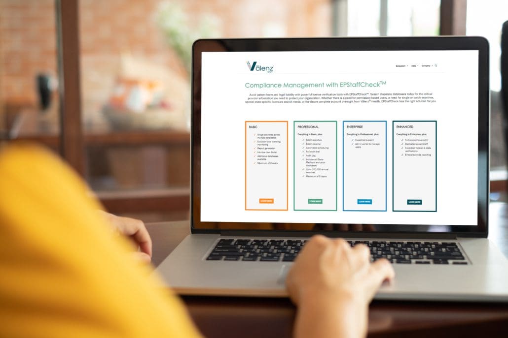 Tablet displaying a Valenz Health compliance management webpage with four package options: Basic, Professional, Enterprise, and Enhanced, each in a colored box.