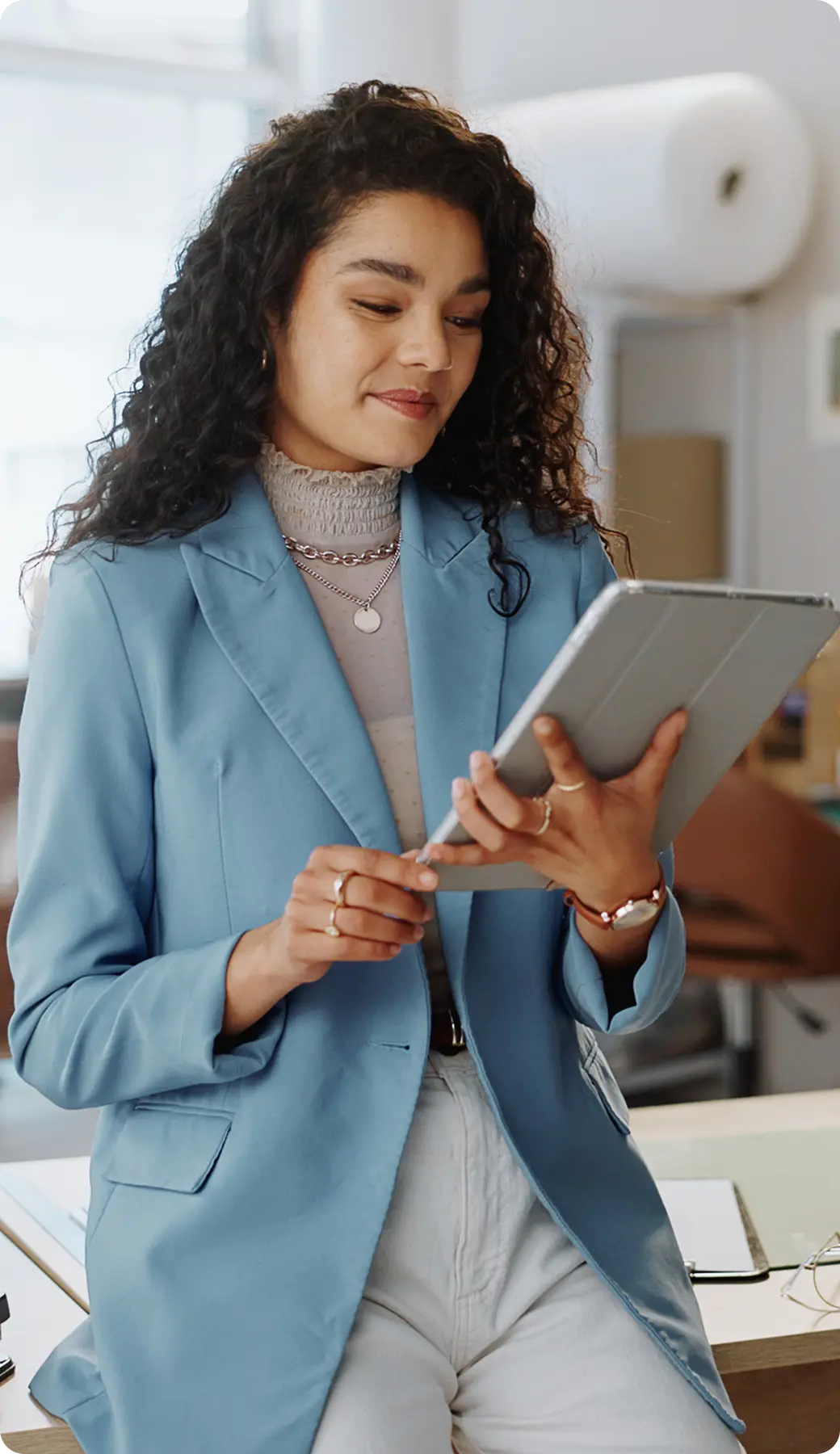 Business-Woman-holding-Tablet A woman in a blue blazer holds and looks at a tablet in a bright office setting.