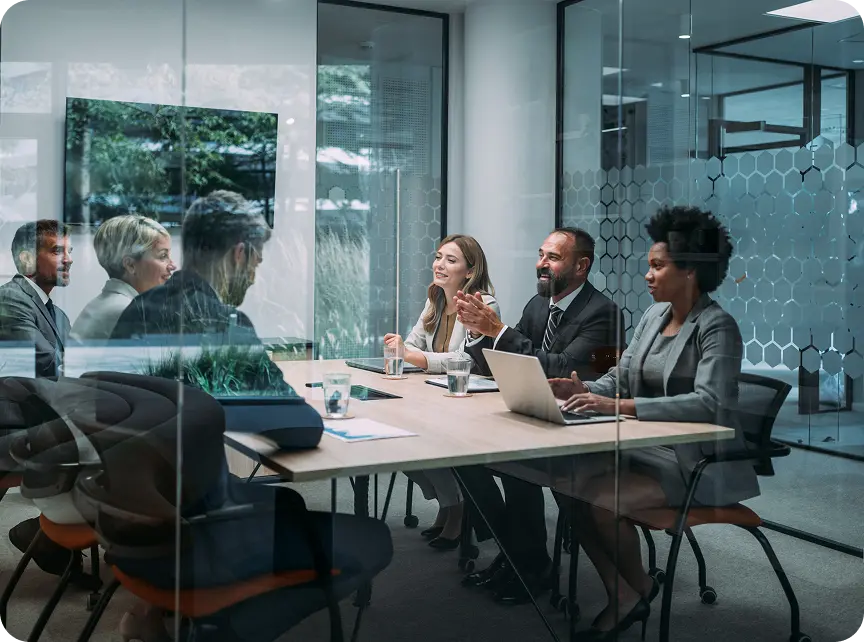 clean-claim-verification-hero Group of business professionals engaged in a meeting in a modern conference room with glass walls.