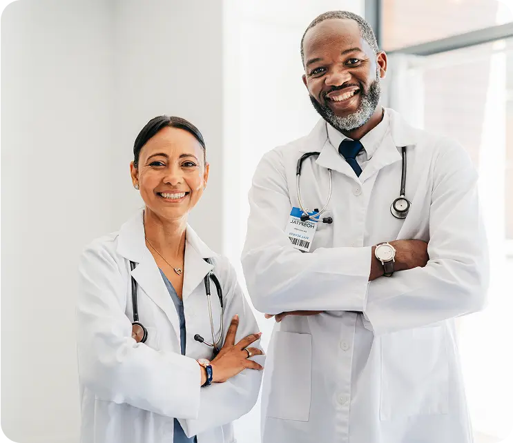 Hero-CareChex-Awards Two doctors smiling and standing confidently, one woman with long black hair in a white coat with a stethoscope around her neck, and one man with short hair and a neatly trimmed beard wearing a white coat and tie, both against a bright, modern background.