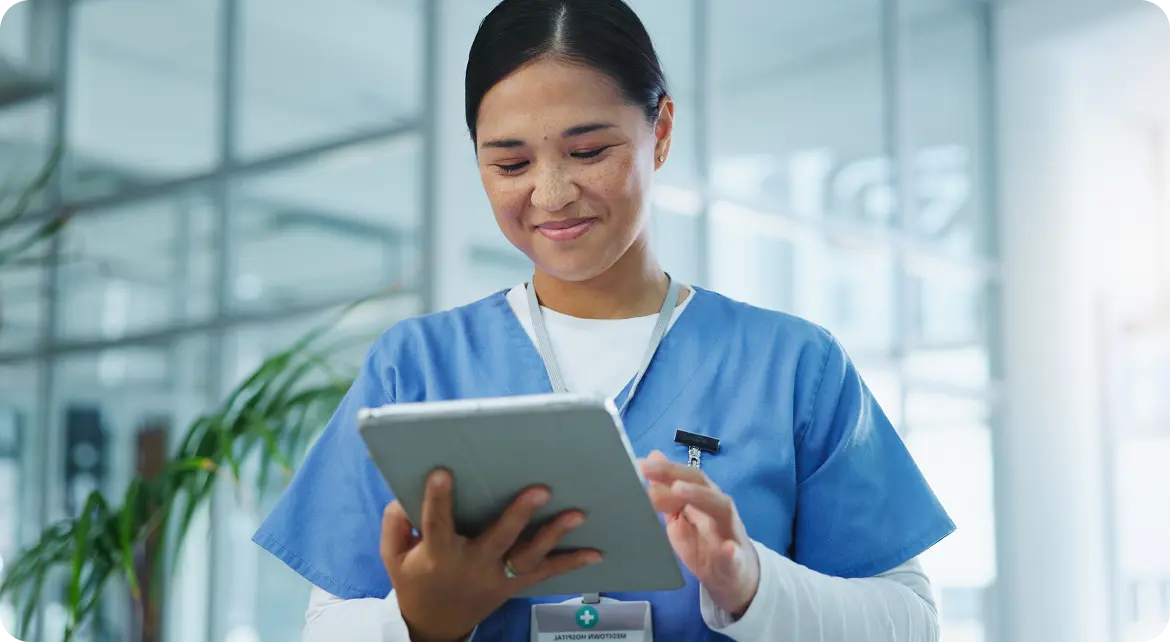 A healthcare professional in blue scrubs using a tablet in a modern medical facility.