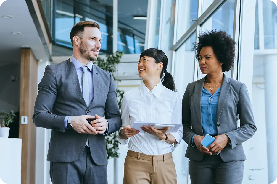 INN-Right-2-1 Three business professionals standing together in an office, with one man and two women, each wearing business attire, smiling and holding electronic devices.